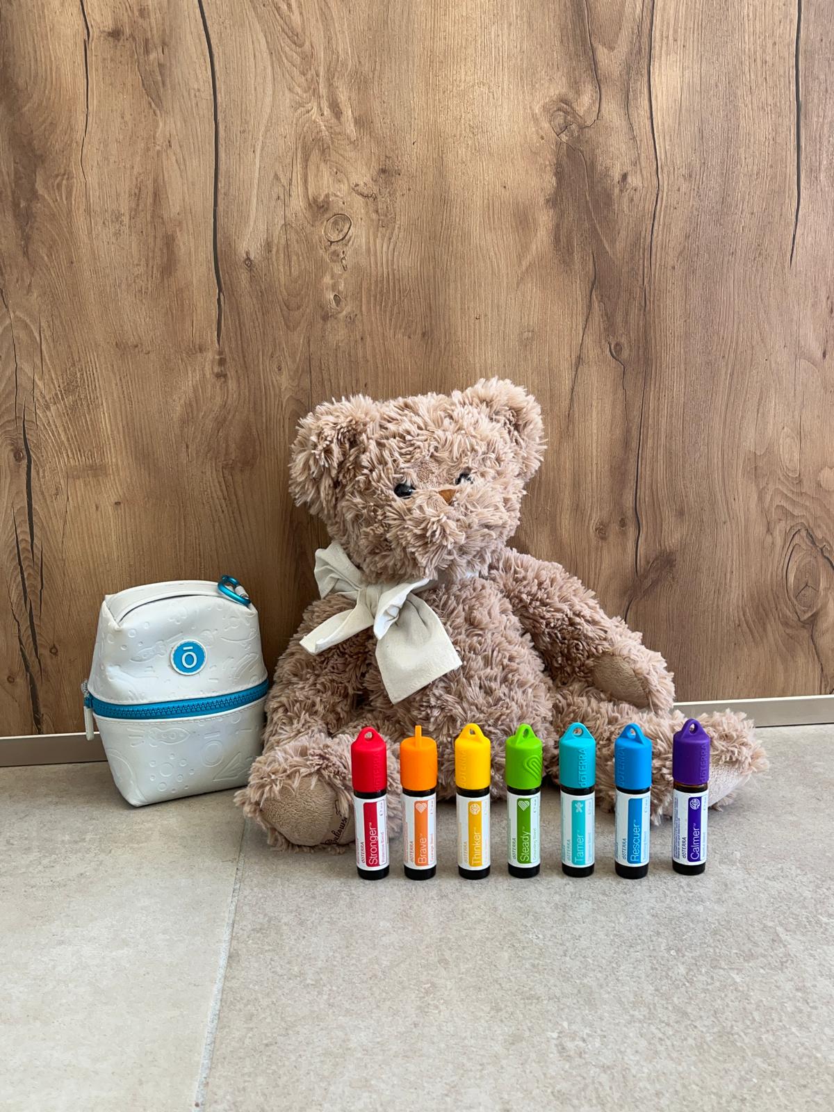 Les 7 roll-on du Kit Enfant doTERRA alignés devant un ourson en peluche, à côté de leur trousse