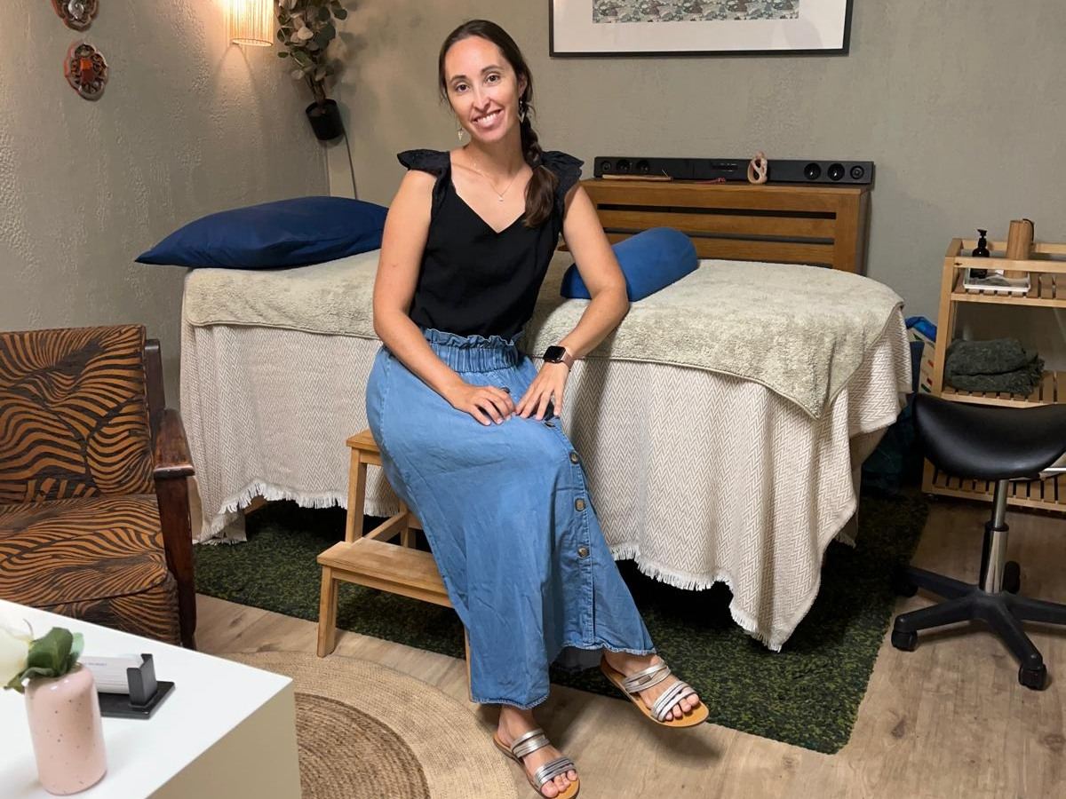 Lucie souriante, assise devant la table de soin de son cabinet
